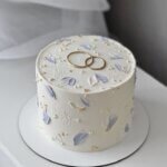 Custom engagement cake Karachi with gold rings topper and lavender floral palette.