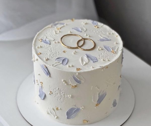 Custom engagement cake Karachi with gold rings topper and lavender floral palette.